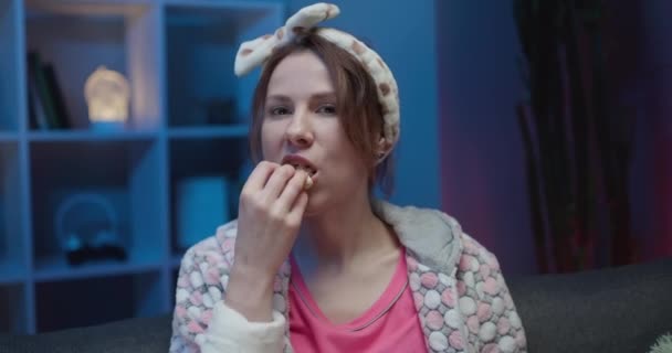 Mujer viendo películas en casa, hembra comiendo palomitas de maíz y mirando la película en el sofá en la sala de estar en concepto de noche . — Vídeo de stock