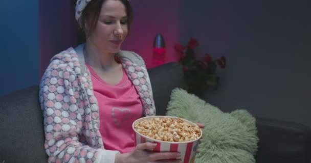 Kvinna tittar på rolig film på tv och äter popcorn på soffan. — Stockvideo