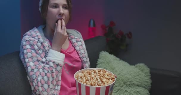 Chica en casa reaccionando a una película nocturna, comiendo palomitas de maíz — Vídeo de stock