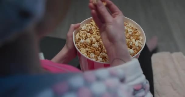 Mano cava en el cubo lleno de palomitas de maíz en busca de la pieza perfecta. Escena en el cine. Mano toma palomitas de maíz de un gran cubo en el cine con una hermosa luz tenue — Vídeos de Stock