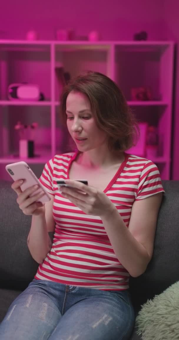 Zbliżenie pięknej młodej kobiety w okularach zakupy online na urządzeniu smartfona, siedząc na kanapie w salonie i trzymając kartę kredytową, a następnie jest bardzo szczęśliwy. — Wideo stockowe