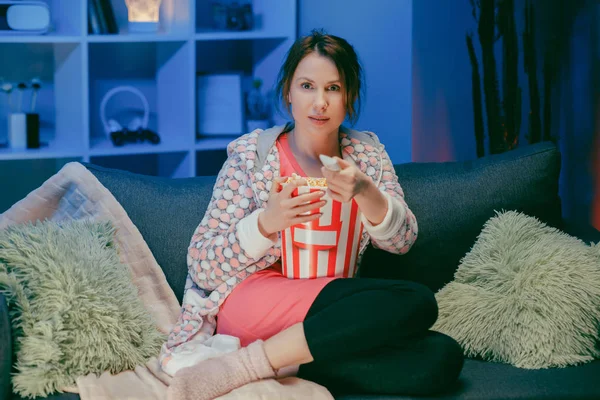 Boldog nő ül a nappaliban kanapé nézi vicces érdekes program és rámutatva megosztása eszik popcorn éjjel. — Stock Fotó