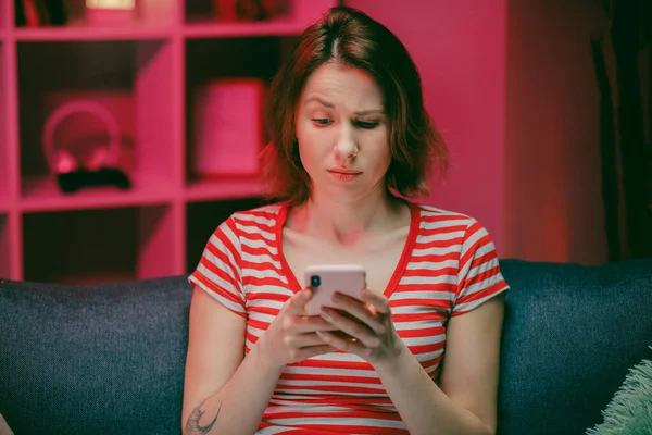 Happy Young Woman Holding Smart Phone Looking at Cellphone Screen Laughing Enjoying Using Mobile Apps for Shopping. Having Fun Playing Games Chatting in Social Media Sit on Couch at Home