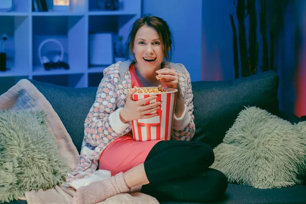 Nő ül a nappaliban kanapé nézi vicces érdekes program és rámutatva megosztása eszik popcorn éjjel — Stock Fotó
