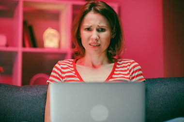 Şok olmuş genç bir kadın dizüstü bilgisayar ekranına bakıyor. Şaşırmış bir kız bilgisayar kullanıyor. İnanılmaz online haberler yazıyor..