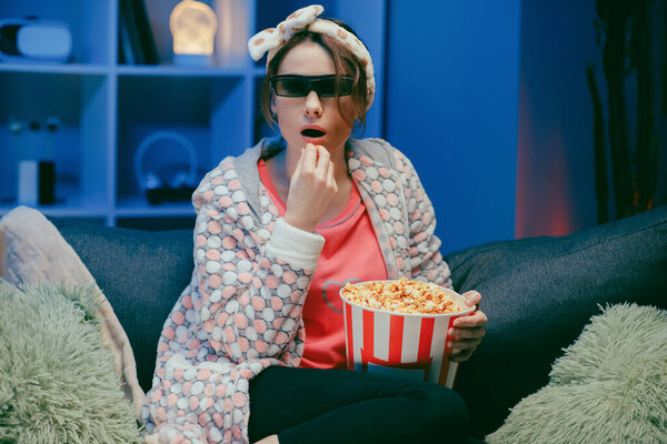 Женщина в 3D очках ест попкорн. Веселая молодая женщина в 3D очках смотрит фильм, ест попкорн. Люди искренние эмоции в кино, образ жизни концепции
.