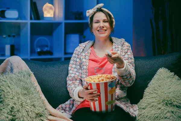 Cheerful casual woman with funny face eating popcorn and looking film sit on sofa enjoy sincere positive emotions screaming with laughter concept
