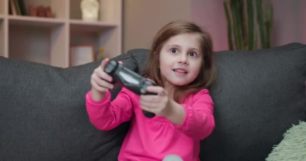 Κοριτσάκι που παίζει σε κονσόλα βιντεοπαιχνιδιών χρησιμοποιώντας χειριστήριο Joystick. Ευτυχισμένο κοριτσάκι που παίζει βιντεοπαιχνίδια — Αρχείο Βίντεο