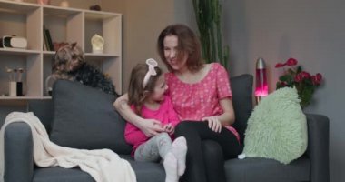 Kadın ve küçük kızı kanepede oturup TV 'de komedi filmi izleyip gülüyorlar.