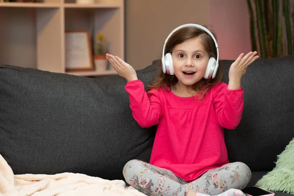 Dziewczynka słucha muzyki na słuchawkach bezprzewodowych. Zabawna dziewczynka tańcząca, śpiewająca i poruszająca się do rytmu. Kid nosi słuchawki. — Zdjęcie stockowe