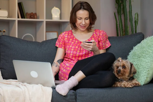 Woman are buying online with a credit card and smile while sitting on the sofa at home. Woman are using laptop and doing online transactions — Stock Photo, Image