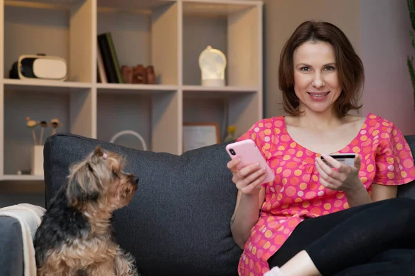 Woman are buying online with a credit card while sitting on the sofa in the living room. Women are using smartphone and doing online transactions. — Stock Photo, Image