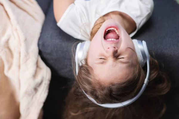 Zabawna dziewczynka w bezprzewodowych słuchawkach tańcząca śpiewająco i poruszająca się w rytm. Dziewczynka w słuchawkach. Dzieciak w słuchawkach. Szczęśliwa dziewczynka słuchająca muzyki ze słuchawkami. — Zdjęcie stockowe