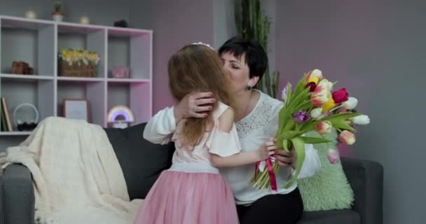 La figlioletta si congratula con la madre anziana per la festa della mamma. Una bambina abbraccia la mamma, le sorride e le dice parole gentili. Baciare e abbracciare una famiglia felice. Buona festa della mamma. Mamma e bambino — Video Stock