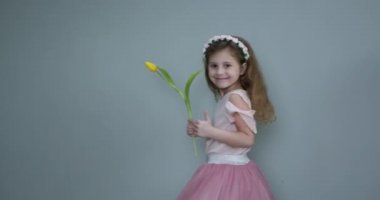 Arka planda çiçek buketi olan kız çocuğu. Küçük kız annesi için sarı lale tutuyor. 8 Mart ya da Anneler Günü konsepti