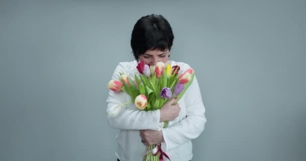 Vrouw die tulpen vasthoudt en glimlacht naar de camera. Mooie vrouw in mooie lente boeket van tulpen. Een vrouw met diverse bloemen. Glimlachende vrouw met bos bloemen — Stockvideo