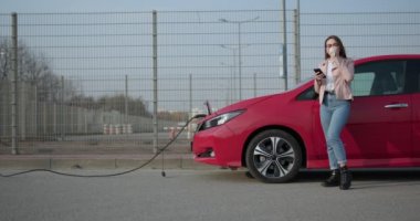 Kadın, akıllı telefon ve güç kaynağı beklerken yeniden kullanılabilir ekolojik saman içeceği kullanır. Arabanın aküsünü şarj etmek için elektrikli araçlara bağlanır..