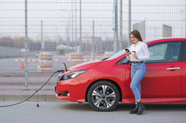 Akıllı Telefon ve Bekleme Güç Aracını Araçların Şarjı İçin Elektrikli Araca Bağlanırken, Kız Kahve İçeceği Kullan.