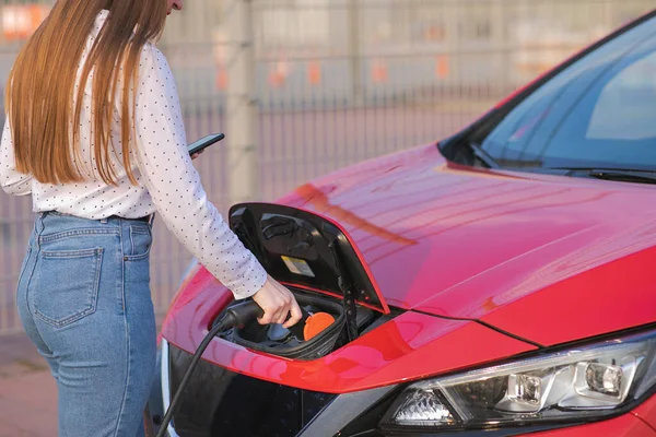 Çevre dostu sıfır emisyonlu elektrikli arabaya kadın eli ekleme gücü kablosu. Kadın şarj olan bir elektrikli arabaya güç kaynağı takıyor..