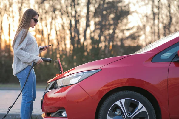 Dívka zapojuje elektrické vozidlo pro nabíjení autobaterie na parkovišti. Připojené nabíjecí kabelové elektrické vozidlo. EV parkoviště, napájecí kabel, nabíjecí stanice — Stock fotografie