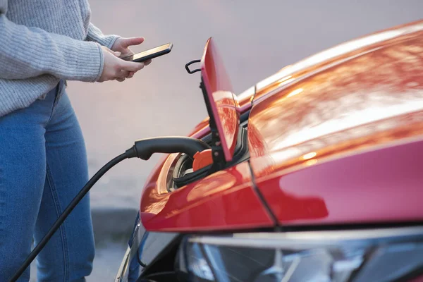 Mujer está enchufando el vehículo eléctrico para cargar la batería del coche en el aparcamiento. De cerca. Cargando coche eléctrico. EV coche conectado al cargador — Foto de Stock