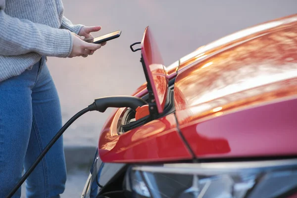 Kadın park yerinde araba aküsünü şarj etmek için elektrikli araç kullanıyor. Kapatın. Elektrikli araba yükleniyor. EV arabası şarj cihazına bağlandı