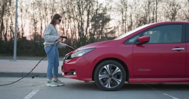 Девушка делает блок питания подключен к электрическому автомобилю заряжается — стоковое видео