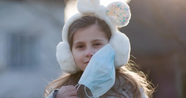 Little girl Takes Off Medical Mask. Isolated on sunset background. Breathes deeply and smiling looking at camera. Health care and medical concept. — Stock Video