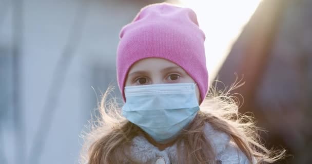 Dívka v masce během epidemie coronaviru COVID-19. Nemocná dívka nosí ochranu během pandemie. Pěkný mladý kavkazský dívka brát na lékařské masky venku. — Stock video