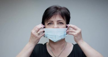 Kıdemli Kadın Tıbbi Maske Takıyor. Derin nefes alıyor ve gri arka plandaki kameraya bakıyor. Sağlık ve tıbbi konsept.