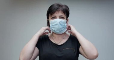 Kadın Tıbbi Maskeyi Çıkartıyor. Gri arka planda izole edilmiş. Derin nefes alıyor ve kameraya bakıp gülümsüyor. Sağlık ve tıbbi konsept.