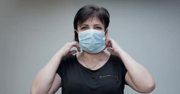 Vrouw doet het medische masker af. Geïsoleerd op grijze achtergrond. Ademt diep en glimlachend kijkend naar de camera. Gezondheidszorg en medisch concept. — Stockvideo