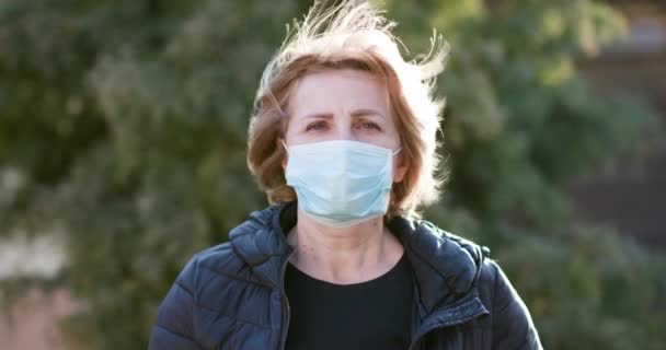 Женщина в медицинской маске во время эпидемии коронавируса COVID-19. Больной женщины, носящей защиту во время пандемии. Красивая белая женщина берет медицинскую маску на открытом воздухе — стоковое видео