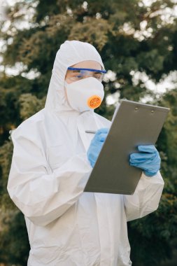 Doktor epidemiyoloji uzmanı Coronavirus COVID-19 ile savaşıyor. Coronavirus Koruma Salgını Tehdit Kapsülü 19. Koruyucu İzolasyon Giysisi ve Maskeli Kadın Verileri Not Defterine Not Ediyor.