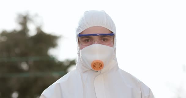 Woman Takes Off Medical Mask Isolated on Green Background Outdoor. Virologist worker in protective suit, goggles and respirator. Covid-19 coronavirus epidemic spreading prevention. — Stock Video