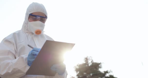 Femme médecin portant un masque et costume se tient dehors au coucher du soleil. L'infirmière porte une combinaison et un masque de protection pendant l'éclosion de COVID19 — Video