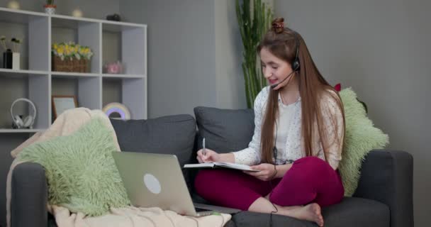 Happy teen school student konferens ringer på datorn för online distansundervisning kommunicera med vän via webbkamera hemma. Leende tonåring flicka bär hörlurar med bärbar dator sittande på sängen. — Stockvideo