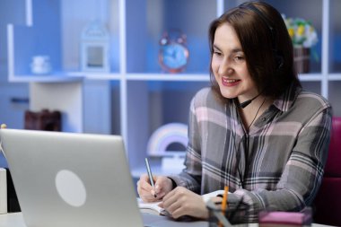 Kız öğrenci internet öğretmeniyle kulaklık çalışması yapıyor. Dil konuşmayı öğreniyor. Laptopa bakıyor..
