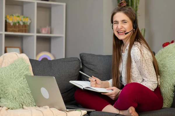 Teenage girl wearing headphones using laptop sitting on bed. Happy teen school student conference calling on computer for online distance learning communicating with friend by webcam at home — Stock Photo, Image