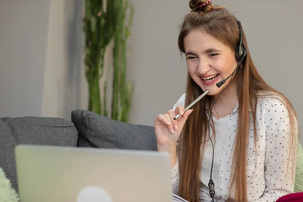 Smiling teen girl wearing headphones listening to audio course using laptop at home, making notes, young woman learning foreign languages, digital self education, studying online — Stock Photo, Image