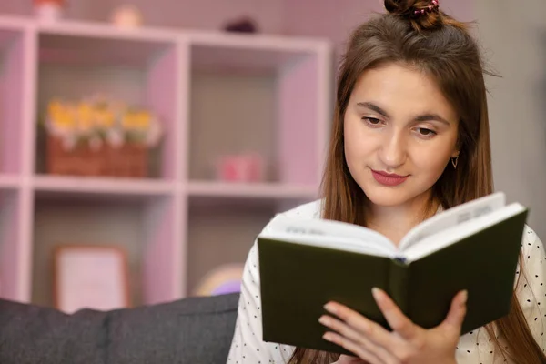 Portret młodego studenta czytającego książkę. Piękna młoda brunetka czyta książkę na łóżku w domu — Zdjęcie stockowe