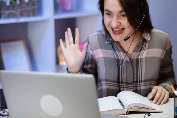 Gelukkige vrouw met koptelefoon begroet tijdens een videoconferentie on line met een rode laptop in een tafel in de woonkamer — Stockfoto