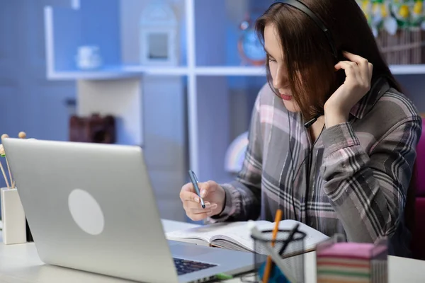 Serious girl student wear headphone study online with internet teacher learn language talk looking at laptop, focused young woman make video call tutoring write notes — Stock Photo, Image