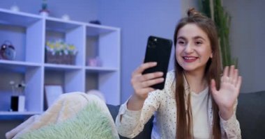 Genç kız blogcu etkileyicisi modern akıllı telefon el sallama selamı veriyor. Gülümseyen vlogger kızı cep telefonuna bakıyor, video çekiyor, selfie çekiyor..
