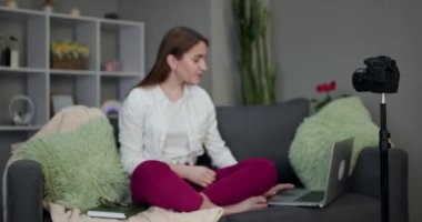Genç kız vlogger evdeki kanepede video yayını yapıyor. İnsanlar ve teknoloji, iş yerinde vlogger olarak çalışan genç bir kadın. İnternet sosyal ağları için web etkileyicisi kayıt iletisi