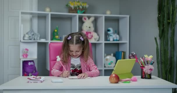 Kleutermeisje kijkt online naar de les en studeert thuis. Kid meisje neemt notities terwijl het kijken naar computer scherm volgende professor doen wiskunde op video oproep. — Stockvideo