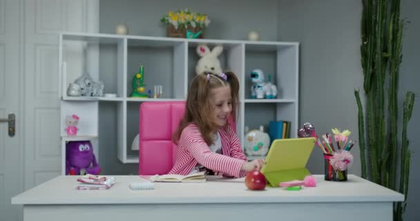 Menina pré-escolar assistindo aula on-line e estudar em casa. Kid girl tomar notas enquanto olha para a tela do computador — Vídeo de Stock