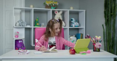 Evde öğrenme kavramı. İnternetteki internet hocası aracılığıyla internet üzerinden kız video araması, çocuk evde oturma odasında otururken ders çalışmak ve günaydın öğretmenini selamlamak.