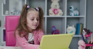Çocuk dijital tablet teknolojisi kullanıyor ve kameraya bakıyor. Küçük çocuk elinde tablet bilgisayarla evde oyun oynuyor. Çocuklar teknoloji bağımlılığı kavramı