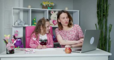 Dizüstü bilgisayarı olan ve okul ödevi yapan liseli kız. Annem evde kızıyla ödev yapıyor. Uzaklık öğrenimi çevrimiçi eğitim.